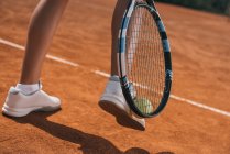 Обрезанный снимок женщины, поднимающей теннисный мяч с ракеткой и ногой — стоковое фото