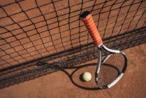 Close-up shot of tennis ball and racket leaning on net — Stock Photo