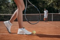 Обрезанный снимок женщины с ракеткой, стоящей над теннисным мячом лежащим на корте — стоковое фото