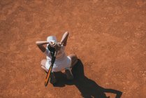 Высокий угол обзора женщины с ракеткой и теннисным мячом, стоящей на коленях на теннисном корте — стоковое фото