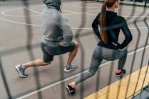 View through fence on sportsman and sportswoman doing lunge exercise — Stock Photo