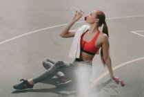 Beautiful sportswoman sitting on ground and drinking water — Stock Photo