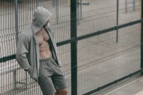 Sportsman standing in unbuttoned hoodie near fence at sports ground — Stock Photo
