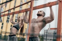 Sportsman and sportswoman pulling up at horizontal bar together — Stock Photo