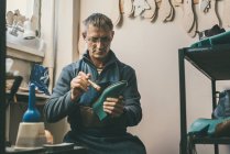 Der gestandene Schuhmacher hält Stiefelwerkstück und arbeitet mit Sohle in seiner traditionellen Werkstatt — Stockfoto