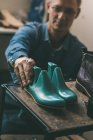Selective focus of shoemaker holding footwear workpieces from shelf in workshop — Stock Photo