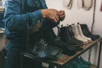 Cropped shot of shoemaker lacing up unfinished leather boots in workshop — Stock Photo