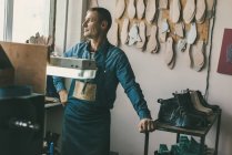 Nachdenklicher Schuhmacher in Arbeitskleidung und Schürze in Werkstatt — Stockfoto