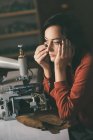 Costureira pensativo olhando para longe enquanto trabalhava com máquina de costura e couro na oficina sapateiro — Fotografia de Stock