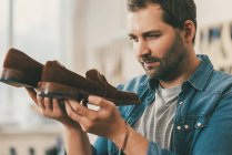 Bearded middle aged shoemaker holding pair of leather shoes — Stock Photo