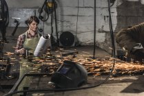 Schweißer mit Tasse Heißgetränk liest Zeitung, während Kollege in Werkstatt arbeitet — Stockfoto