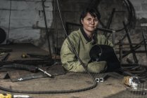 Portrait of smiling female welder with protective helmet in hands in workshop — Stock Photo