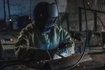 Ручной рабочий в защитном шлеме с сварочной горелкой, работающий в цехе — стоковое фото