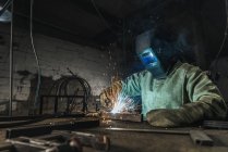 Trabajador manual en casco protector con antorcha de soldadura trabajando en taller - foto de stock