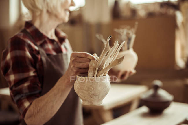 Seniorin hält Schalen mit Töpferwerkzeug in Werkstatt — Stockfoto