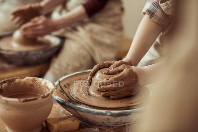 Primer plano de las manos de los niños que trabajan en la rueda de cerámica en el taller - foto de stock