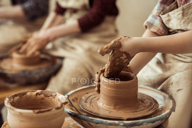 Primer plano de las manos de los niños que trabajan en la rueda de cerámica en el taller - foto de stock