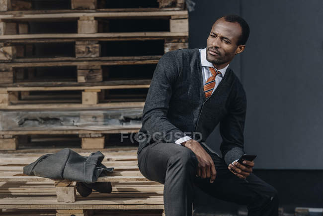 Stanco elegante uomo d'affari afro-americano utilizzando smartphone e seduto all'aperto — Foto stock