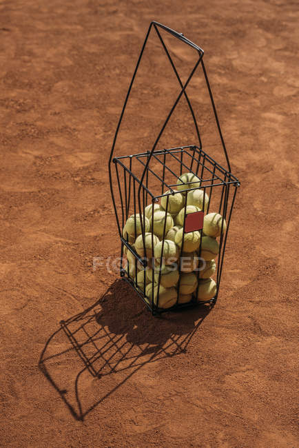 Basket of tennis balls standing on orange court surface — Stock Photo