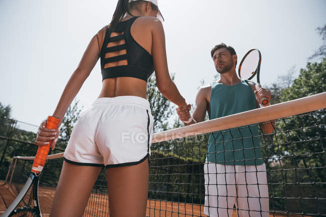 Jeune homme et femme serrant la main avant le match de tennis — Photo de stock