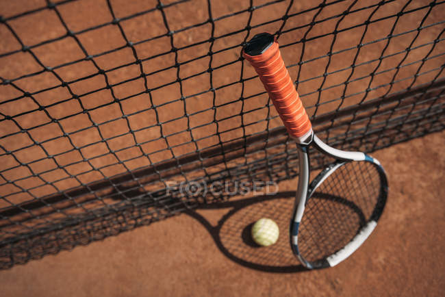 Close-up shot of tennis ball and racket leaning on net — Stock Photo