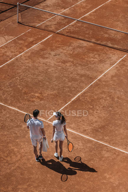 Vue grand angle du couple sportif avec raquettes marchant sur le court de tennis — Photo de stock