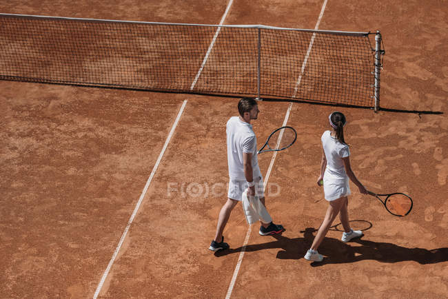Висока кут зору молода пара з ракетки ходьба тенісний корт — стокове фото