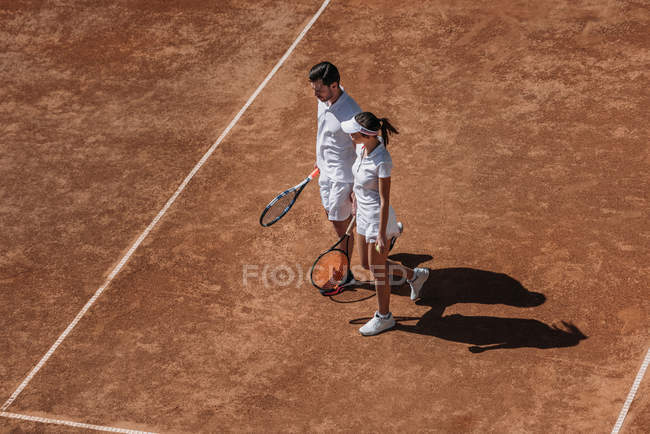High angle view of young sportive couple with rackets walking by tennis court — Stock Photo
