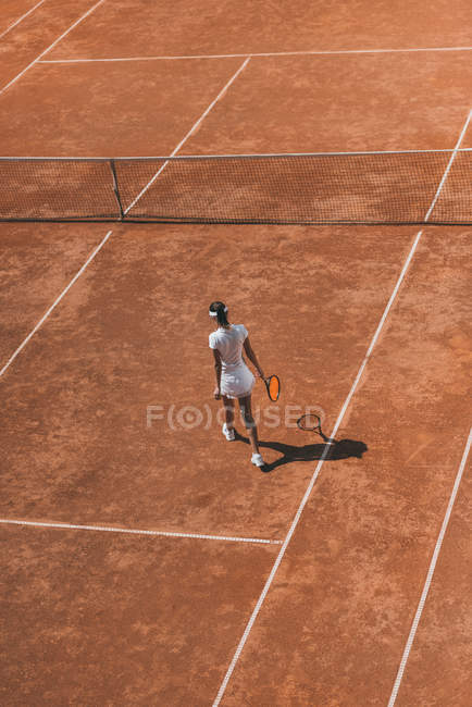 Vue grand angle de la femme en vêtements de sport avec raquette marchant sur le court de tennis — Photo de stock