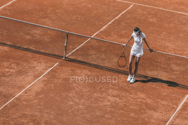 Высокий угол зрения женщины расслабляясь на теннисном корте после матча и опираясь на сетку — стоковое фото