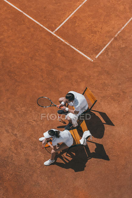 Blick aus der Vogelperspektive auf ein junges Paar, das es sich nach einem Tennismatch auf Stühlen gemütlich macht — Stockfoto