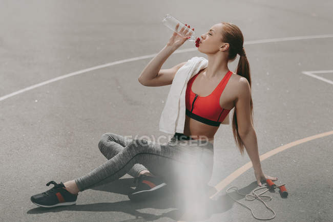 Bela esportista sentado no chão e água potável — Fotografia de Stock