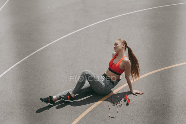 Вид сверху на красивую спортсменку, сидящую на земле и отдыхающую после тренировки — стоковое фото