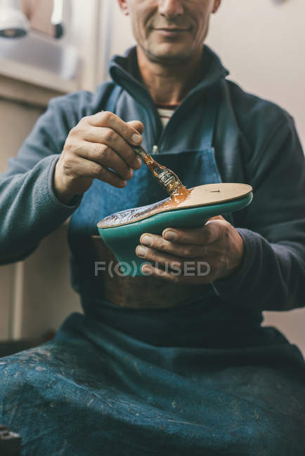 Tiro recortado de zapatero maduro sosteniendo pieza de trabajo de la bota y trabajando con suela en su taller tradicional - foto de stock