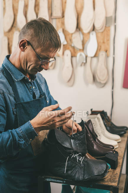 Calzolaio maturo mettendo lacci delle scarpe in stivali non finiti in officina — Foto stock
