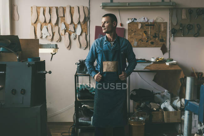 Guapo zapatero adulto en ropa de trabajo y delantal en el taller - foto de stock