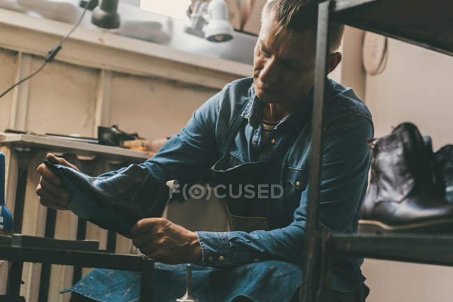 Mature shoemaker holding unfinished leather boot at workshop — Stock Photo