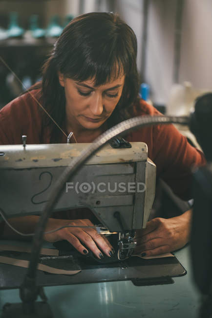 Concentrated mature seamstress working with electrical sewing machine in tailor shop — Stock Photo
