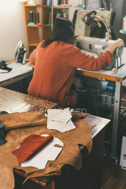 Costureira trabalhando com máquina de costura na loja sob medida com folhas de couro na mesa — Fotografia de Stock