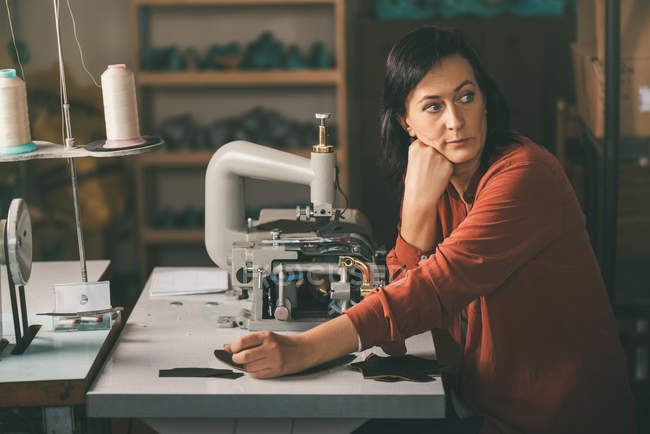 Mature thoughtful seamstress sitting at workplace in tailor shop — Stock Photo