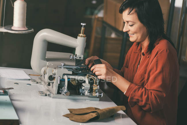 Lächelnde ältere Näherin näht Leder auf elektrischer Maschine — Stockfoto