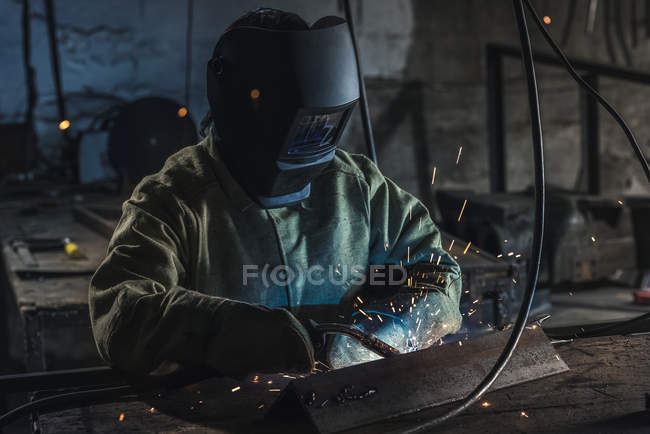 Manual worker in protective helmet with welding torch working in workshop — Stock Photo