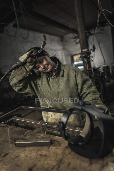 Tired female welder holding welding torch in workshop — Stock Photo