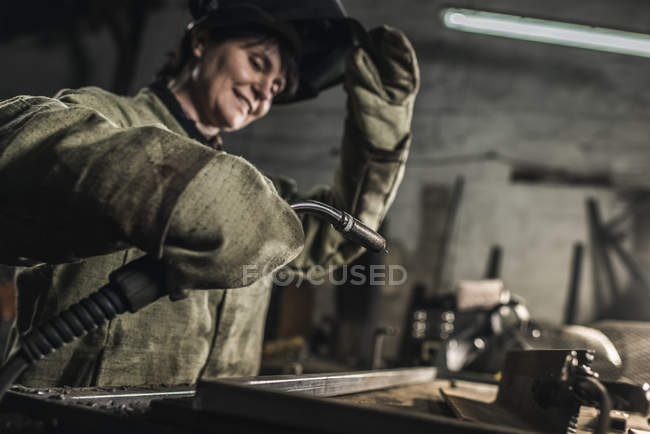 Selective focus of female welder in protective work wear working in workshop — Stock Photo