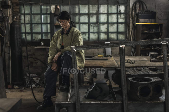 Tired female welder sitting on table while having rest during work — Stock Photo