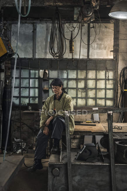Tired female welder sitting on table while having rest during work — Stock Photo
