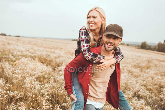 Glückliche junge Frau huckepack auf Freund in Blumenfeld — Stockfoto