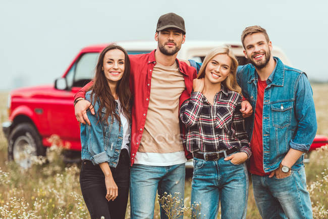 Group of young people embracing and looking at camera in flower field — Stock Photo