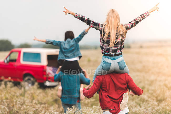 Vista posteriore di giovani donne che cavalcano su fidanzati spalle in campo — Foto stock