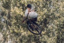 Sportler springt mit Fahrrad mit Bäumen vor verschwommenem Hintergrund — Stockfoto